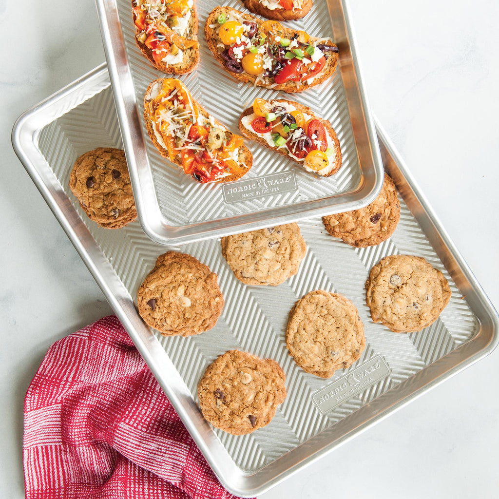 Two nested baking trays with chevron pattern, filled cookies and mini pizzas