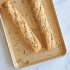 Tan jelly roll sheet pan holding two baked bread rolls with seeds