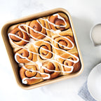 Square nonstick cake pan filled with frosted cinnamon rolls, light tan color