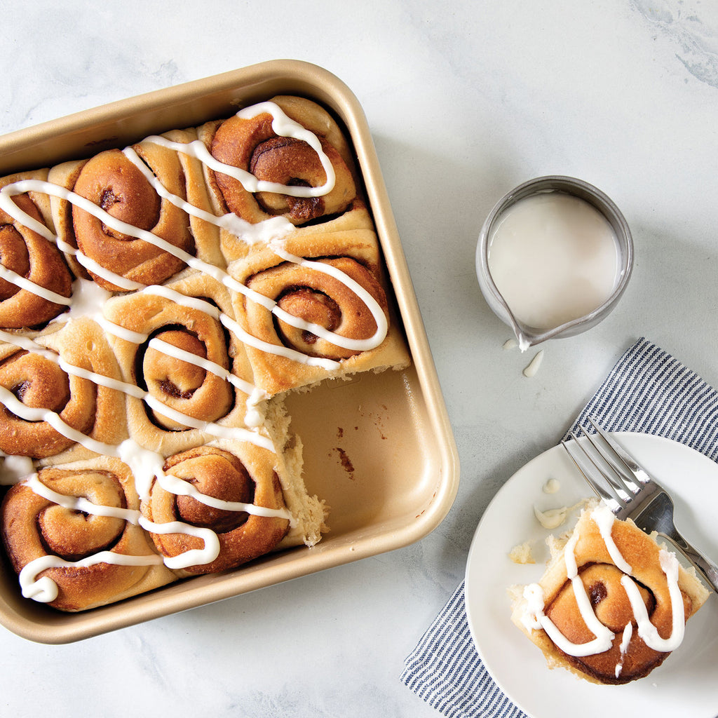 Square nonstick cake pan with sliced frosted cinnamon rolls and crumb topping