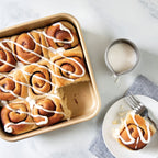 Square nonstick cake pan with sliced frosted cinnamon rolls and crumb topping