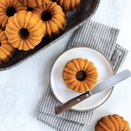 Mini bundtlette cake in a dark pan, with another cake on a white plate