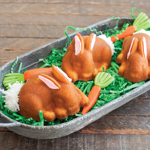 Bunny cakelets on a metal tray, brown with pink ears over green shredded garnish