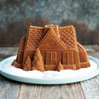 Round plate with dark gingerbread house bundt cake, textured sides, and dusted sugar
