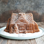 Powdered sugar gingerbread house bundt cake on white plate with embossed door and windows