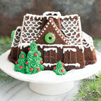 Gingerbread house bundt cake with green frosting trees, white icing roof, and sprinkles