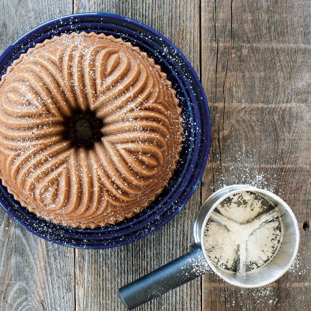 Golden-brown ridged Bundt cake in blue pan with powdered sugar nearby.
