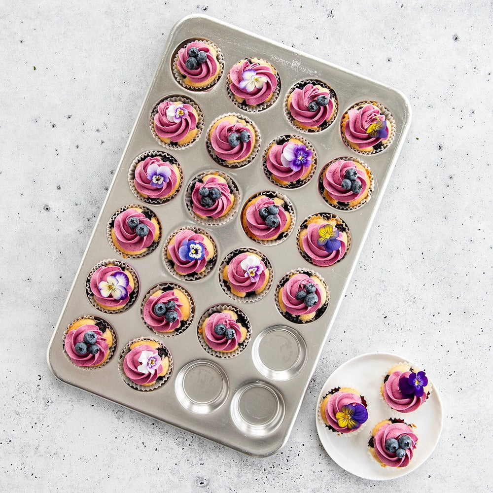 Petite cupcake tray filled with pink swirled frosting cupcakes and two on plate